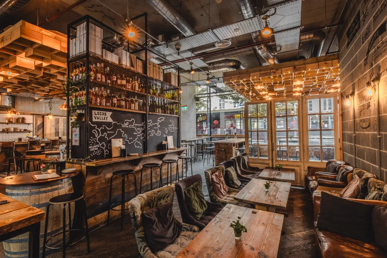 Armchairs and sharing tables beneath a wine-region map above the bar at Vagabond Victoria