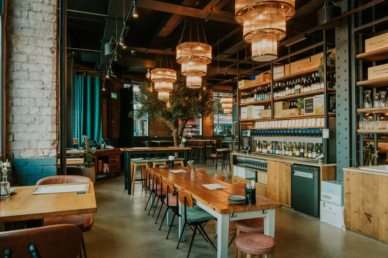 Tables and pink chairs by the self-pour wine machines at Vagabond Birmingham, under glass chandeliers