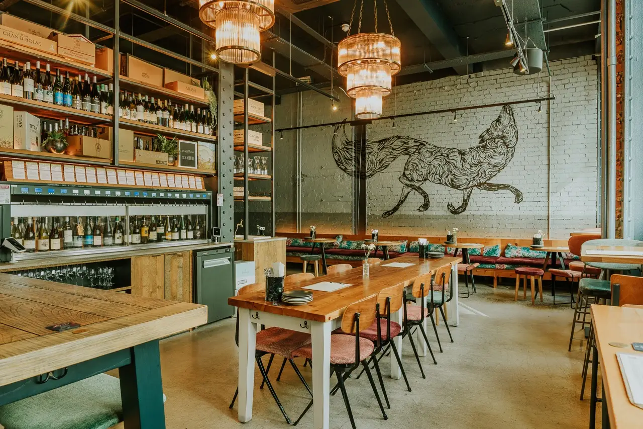 Long sharing tables beneath a fox mural on the white brick wall at Vagabond Birmingham