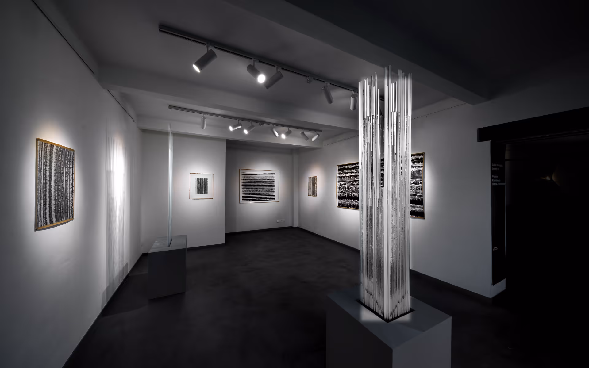 Umělecká galerie s abstraktními černobílými obrazy a moderní skleněnou instalací uprostřed.