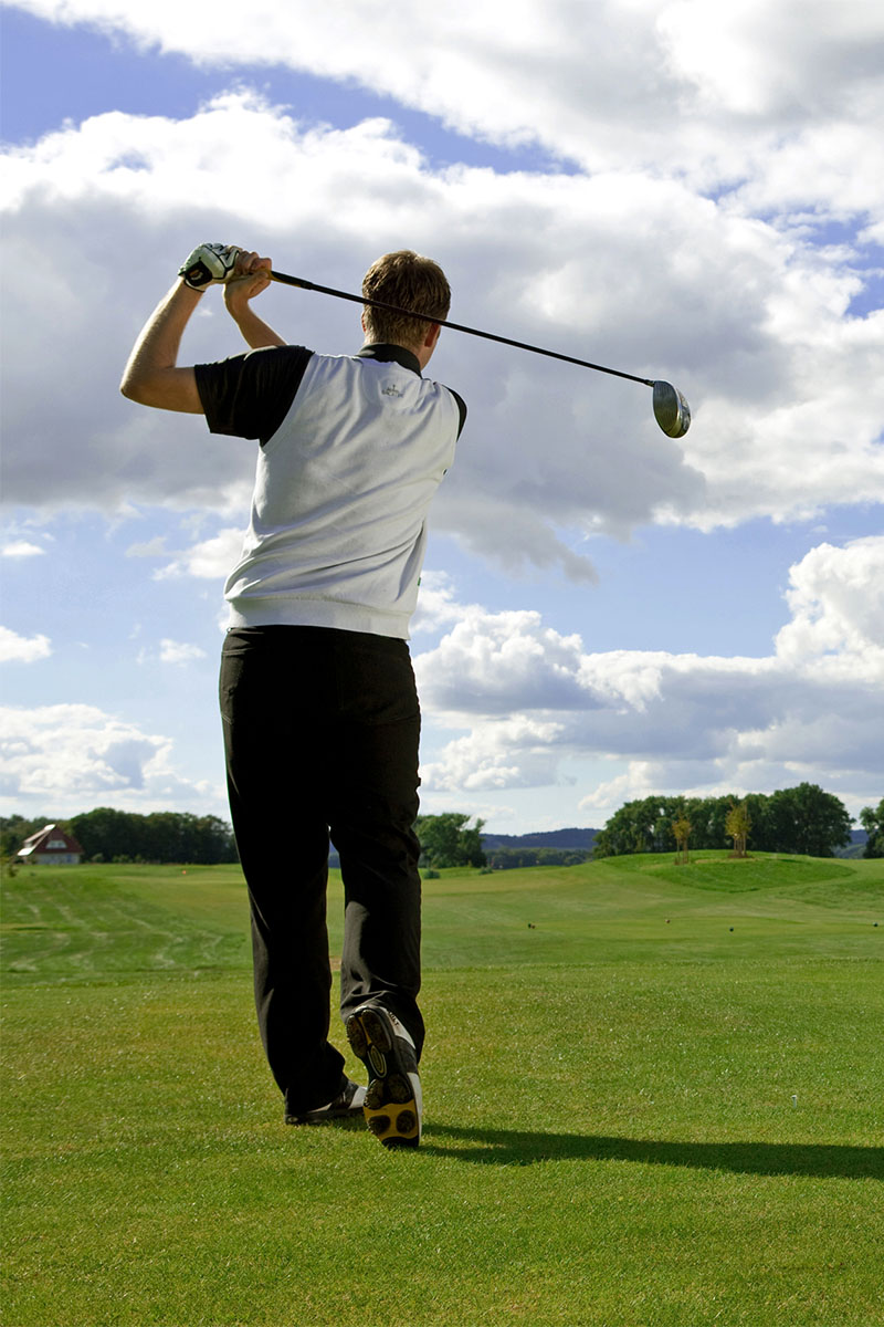 Golfer im Durchschwung mit Blick über die weite Golfanlage des Golfclub Schloss Teschow