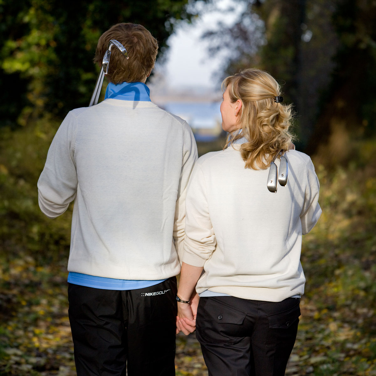 Paar mit Golfschlägern spaziert durch herbstliche Allee, Golfurlaub und Gutscheine im Golfclub Schloss Teschow