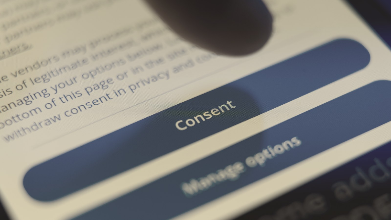 Detail prstu nad tlačítkem Consent v cookie liště na displeji telefonu