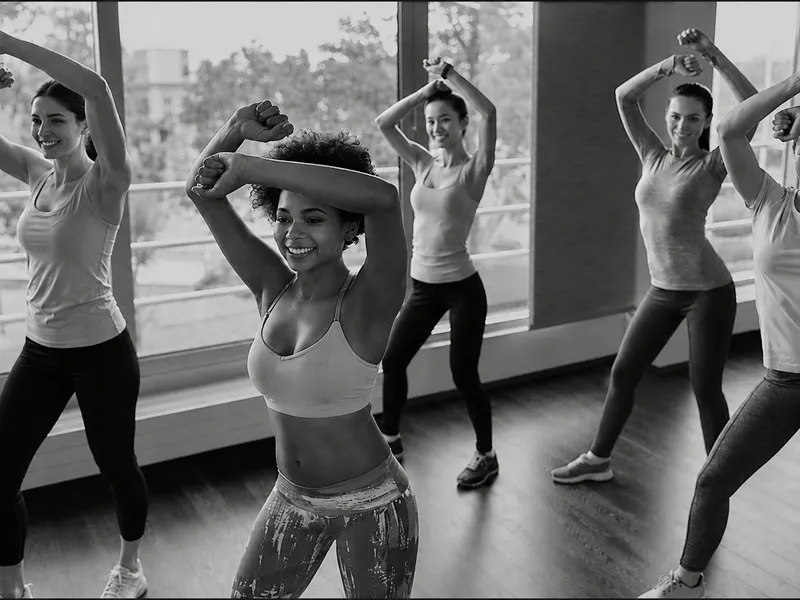 A group of women participates in a fitness class, stretching and exercising together in a bright studio with large windows. Black-and-white image with an energetic and positive atmosphere.