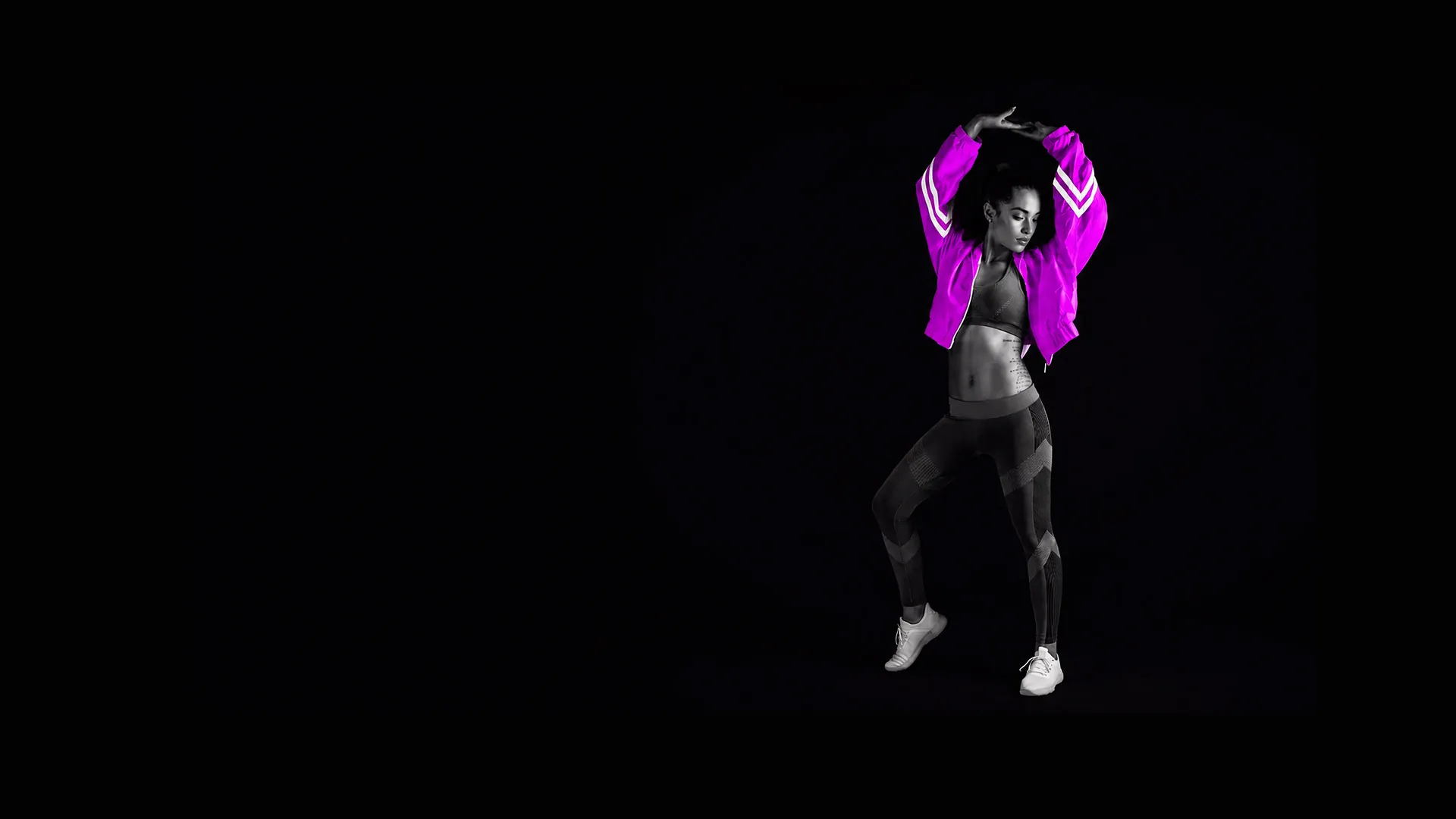 Woman in black and white workout clothes wearing a bright purple jacket poses against black background.