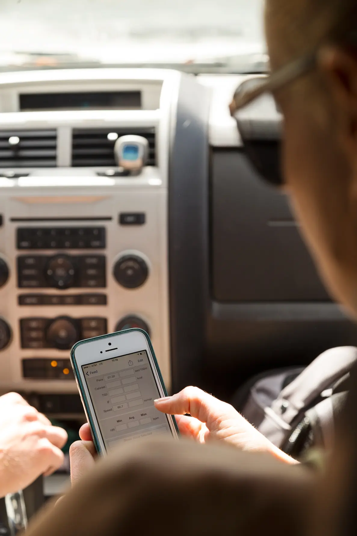 Helle Frederiksen holding smartphone displaying a data input form inside a car dashboard.