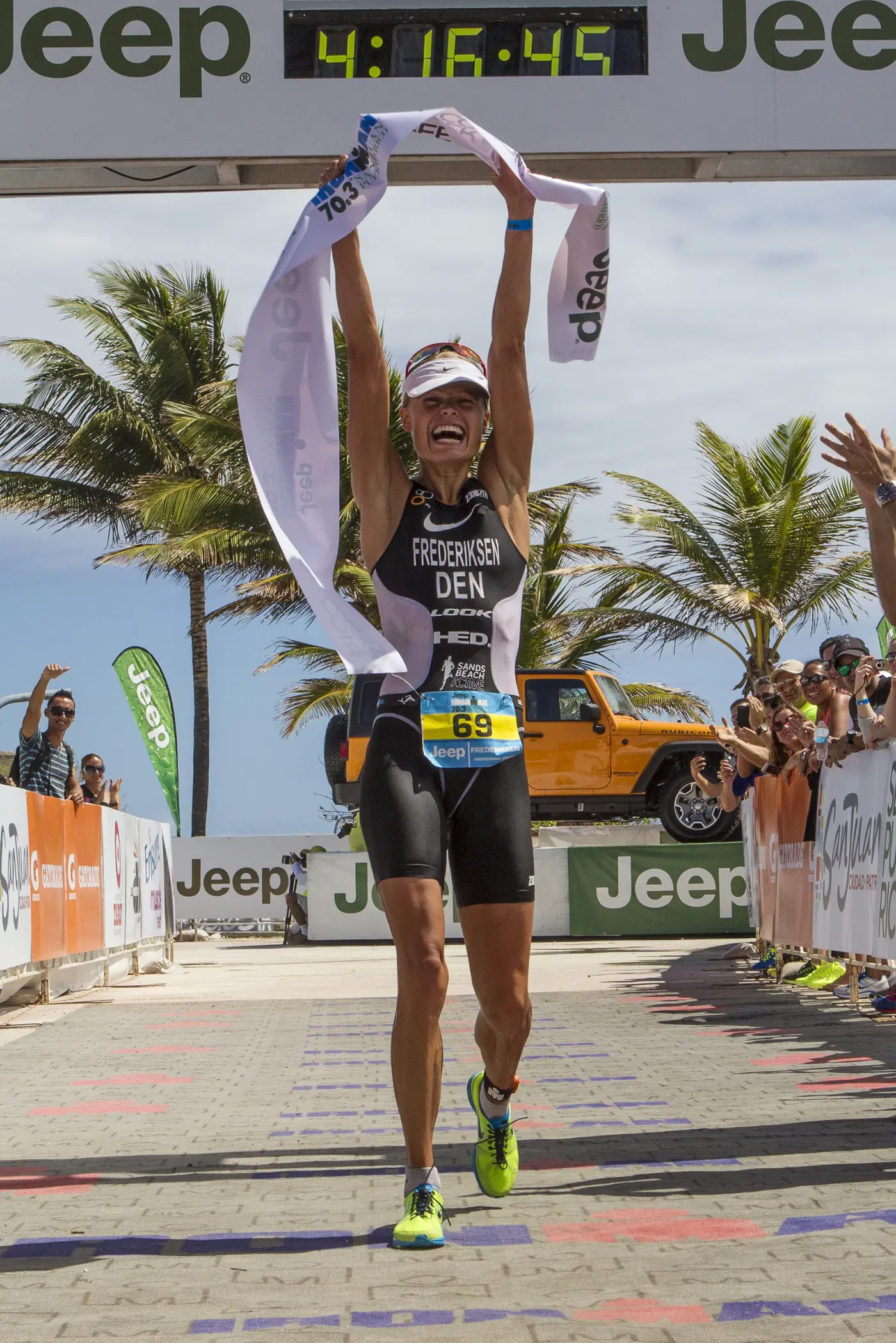 Athlete Helle Frederiksen crossing the finish line victoriously at a Jeep-sponsored race with the timer showing 4:16:45.