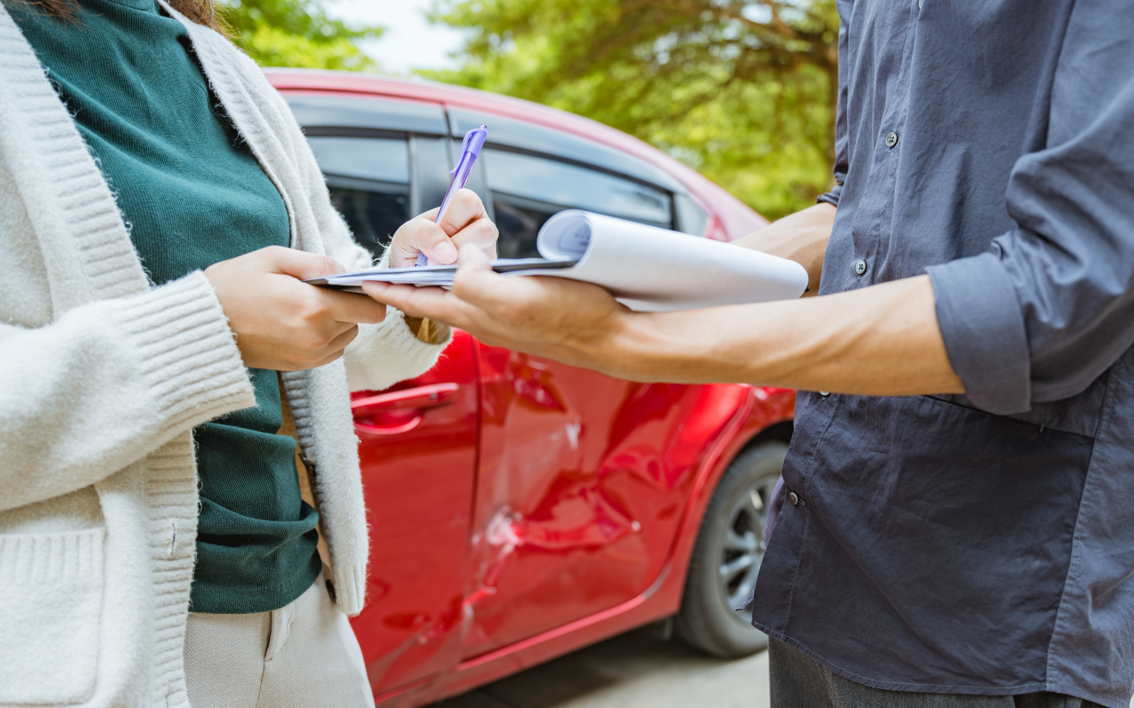 People writing a car accident statement beside a damaged car