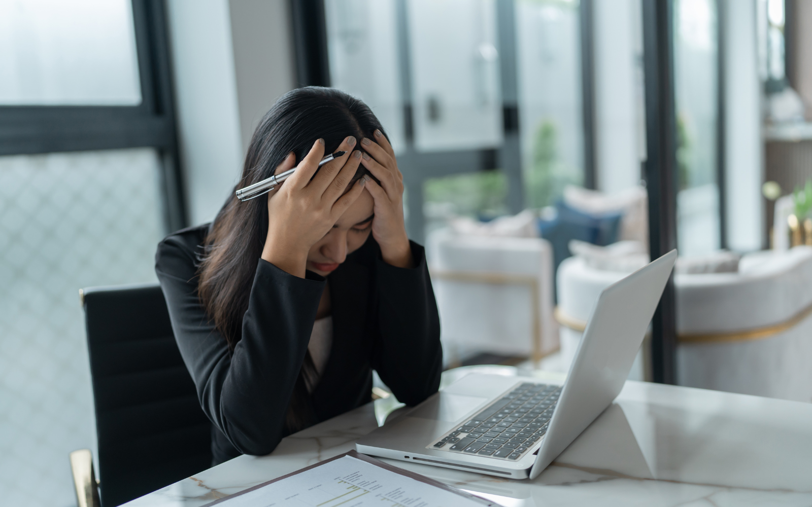 Broker working on financial documents at a laptop with a stressed expression
