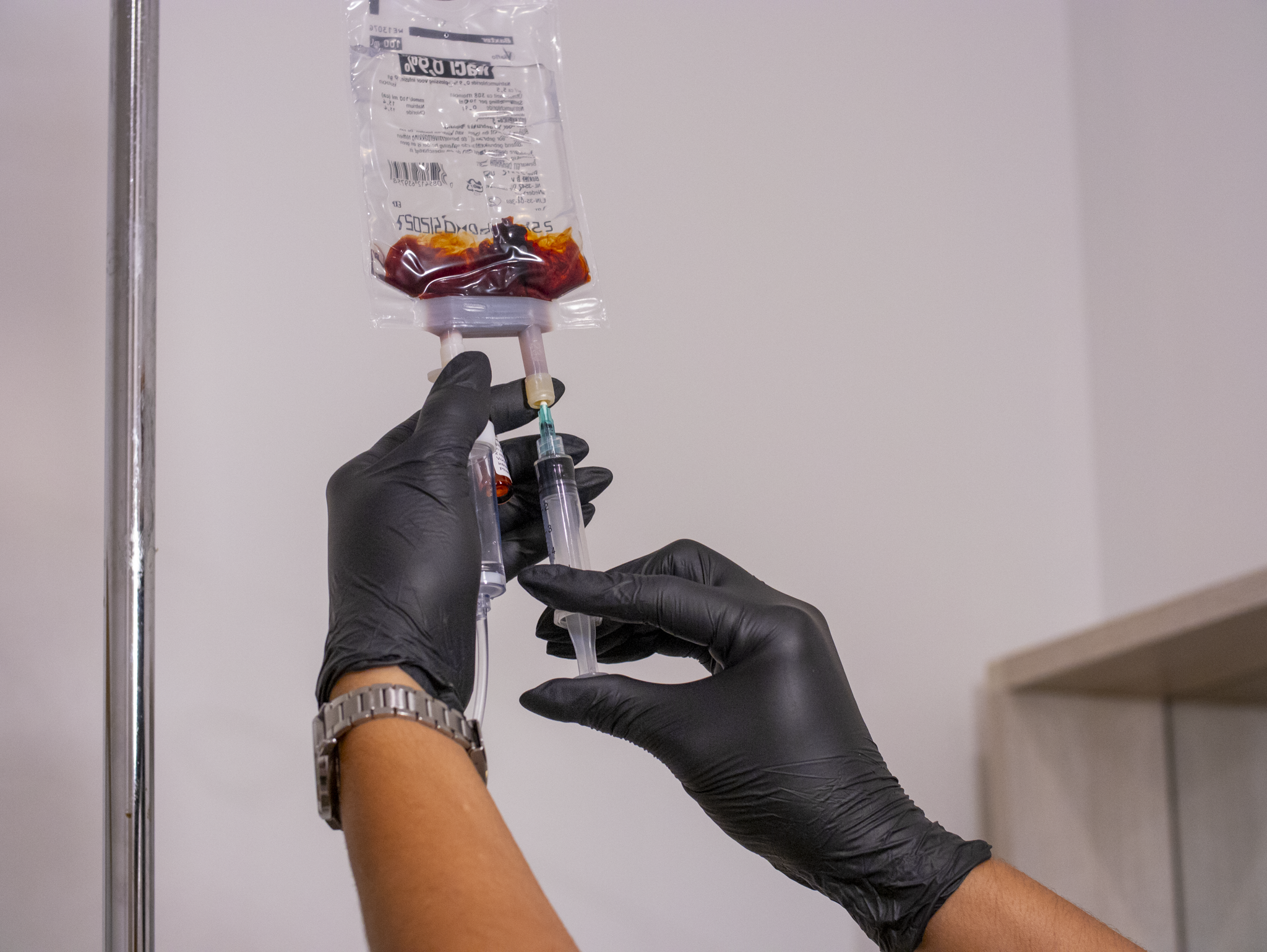 Hands in black gloves holding syringe and intravenous blood bag for medical use.