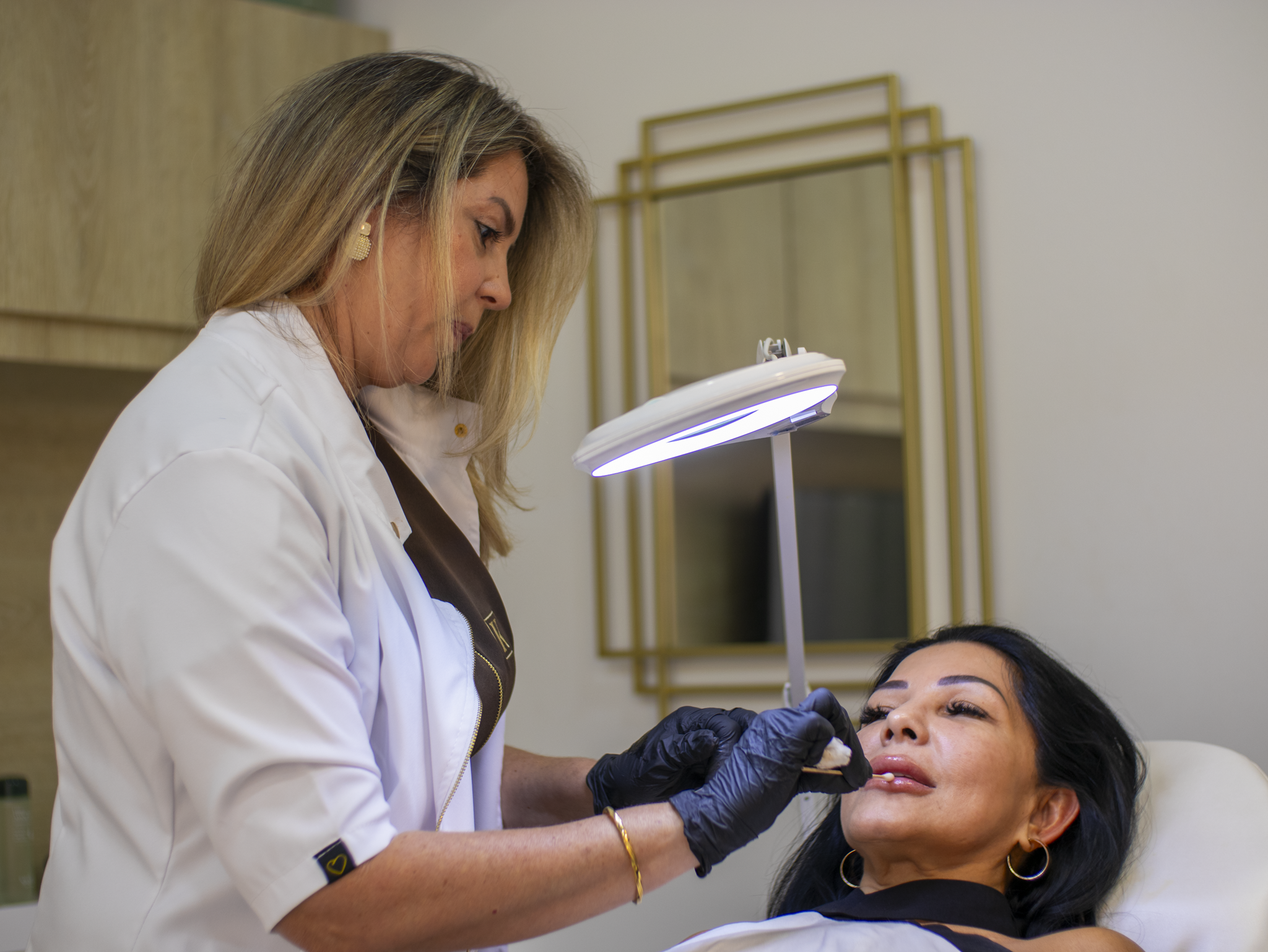 Medical professional wearing gloves examining a woman's lips under a bright ring light.
