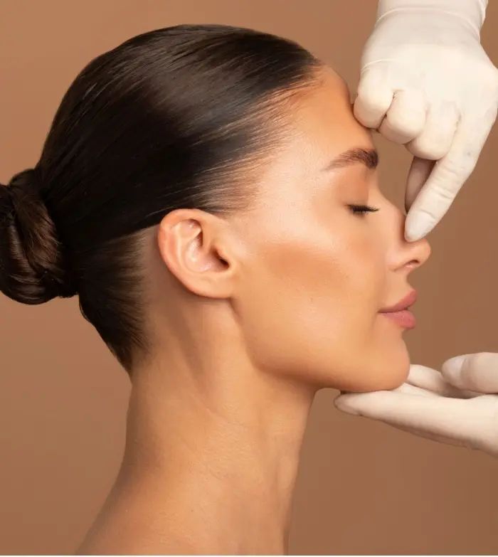 Profile of a woman with eyes closed and hands in gloves touching her nose and chin, against brown background.