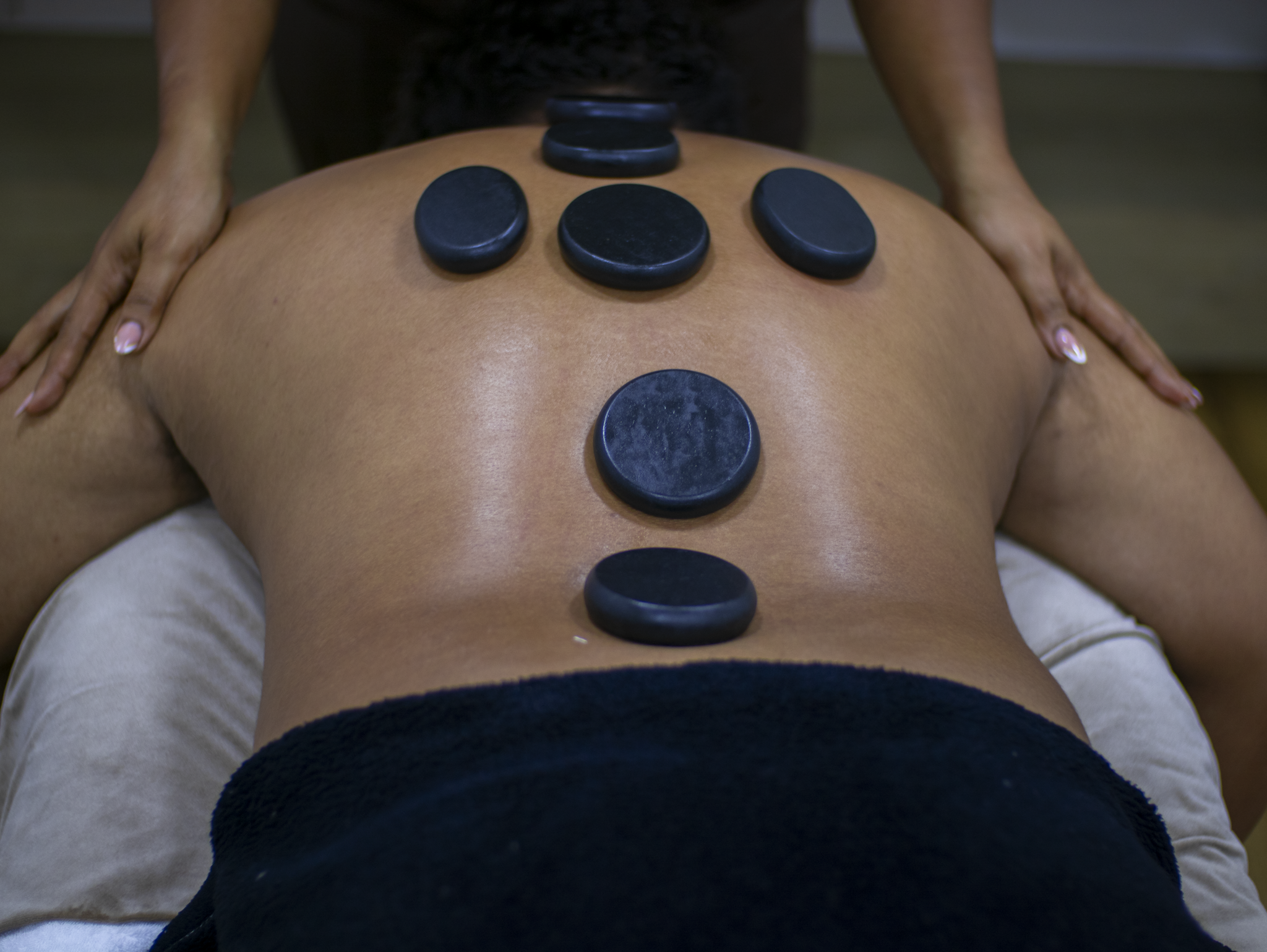 Person lying face down with black hot stones on their back during a massage therapy session.