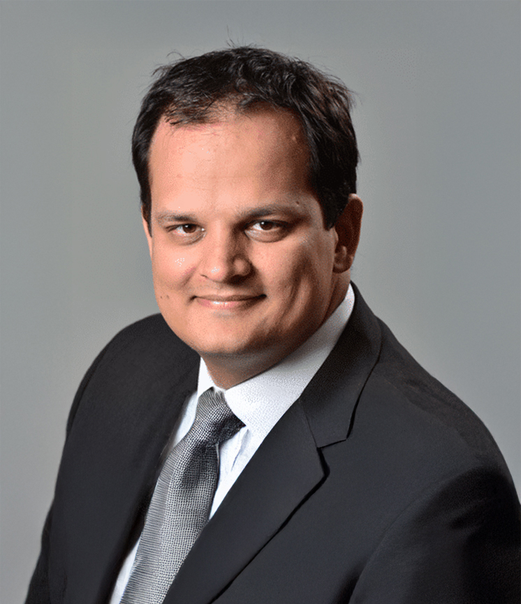 Portrait of a man wearing a black suit, white shirt, and gray tie against a gray background.