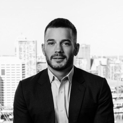 Black and white portrait of a man in a suit jacket and collared shirt with a city skyline behind him.