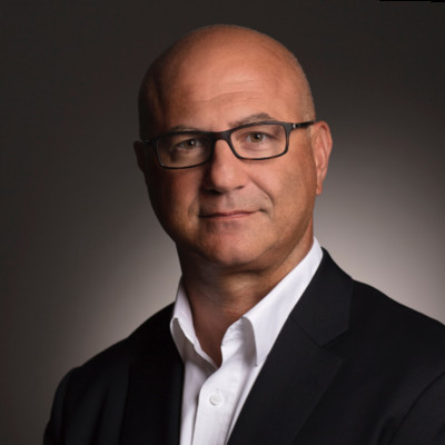 Professional headshot of a bald man wearing glasses, a white shirt, and a black blazer.