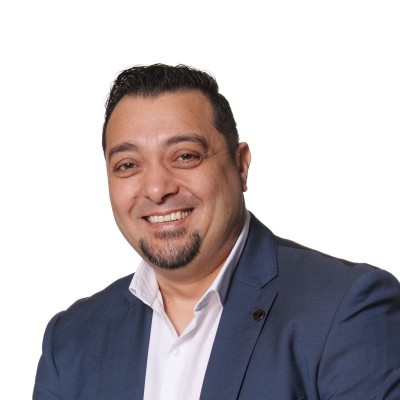 Smiling man with short dark hair and goatee wearing a blue blazer and white shirt on a white background.