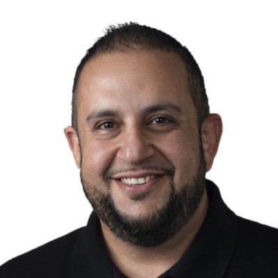Smiling man with short hair and beard wearing a black collared shirt on white background.