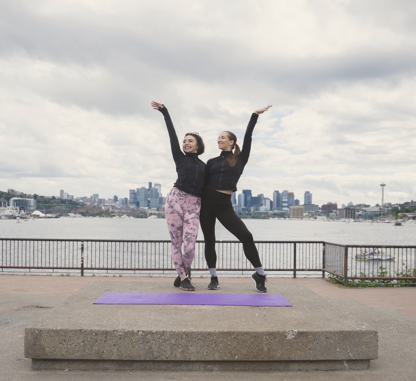 Two women stretching outdoors on the Seattle waterfront, part of the Move Your Body™ community