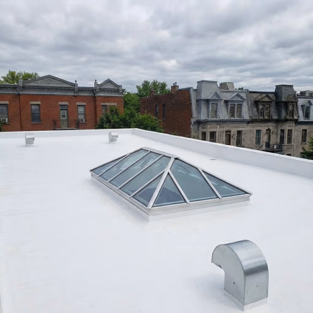 White flat roof with a glass pyramid skylight and metal ventilation ducts, with brick and stone buildings in the background under a cloudy sky.