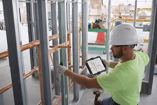 MEP worker using laser projection to mark plumbing pipe routing on a concrete floor during field layout for a commercial building project