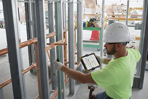 MEP worker using laser projection to mark plumbing pipe routing on a concrete floor during field layout for a commercial building project