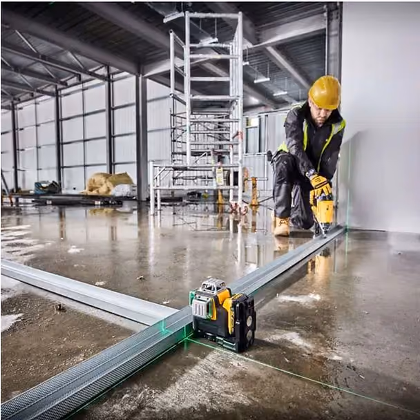 Green laser level on construction site framing project with worker in hard hat aligning metal beams on wet concrete floor"