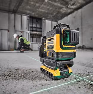 Yellow DeWalt laser level projects green lines on a construction site floor. A worker in a helmet and vest sets up in the background.