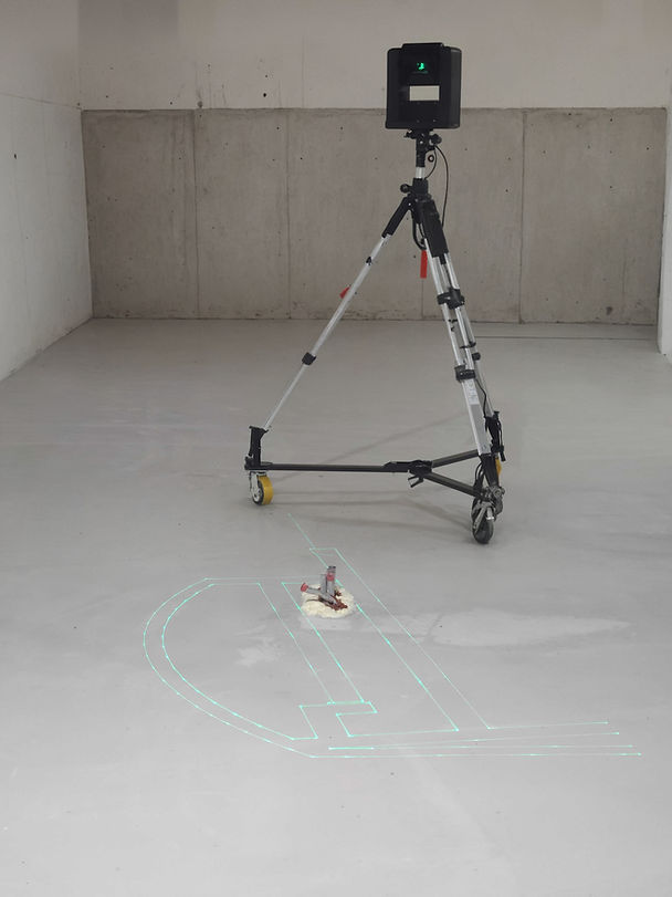 A laser on a tripod projects green lines on a bare concrete floor in a minimalist room with white walls and a gray background.