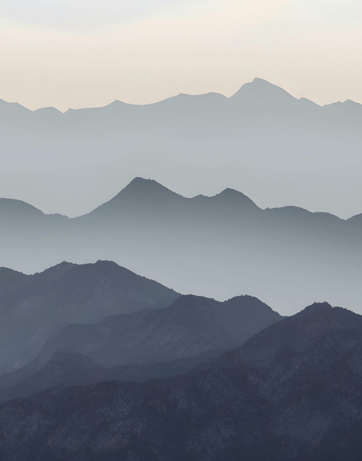 Layered mountain ranges under a soft orange sky at dawn or dusk.