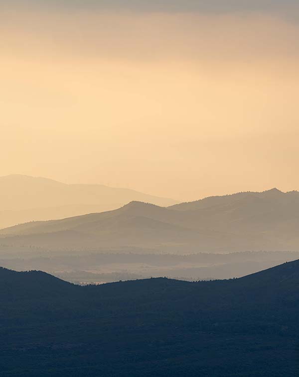 Layered mountain ranges fading into the distance under a soft, warm beige sky.