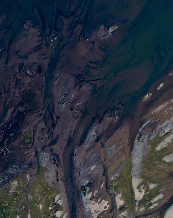Aerial view of a river delta with dark water channels and surrounding muddy and sandy terrain.