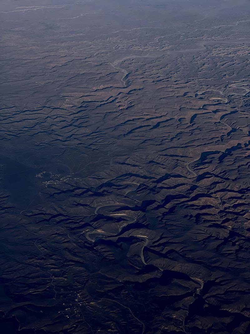 Aerial view of a winding river flowing through a rugged, mountainous landscape with deep shadows and sparse vegetation.