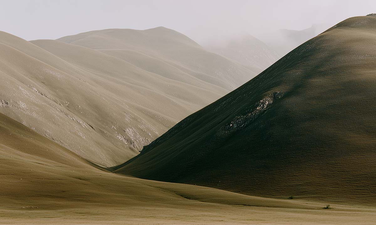 Rolling hills with subtle vegetation under a hazy sky in a mountainous landscape.