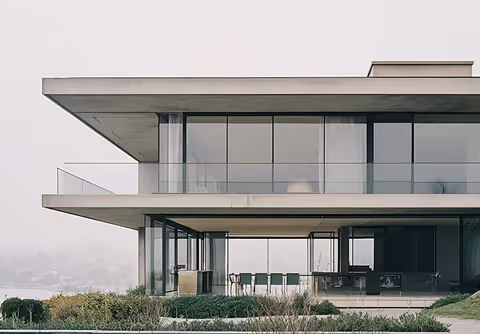 Modern two-story house with large glass windows and balconies overlooking a foggy landscape.