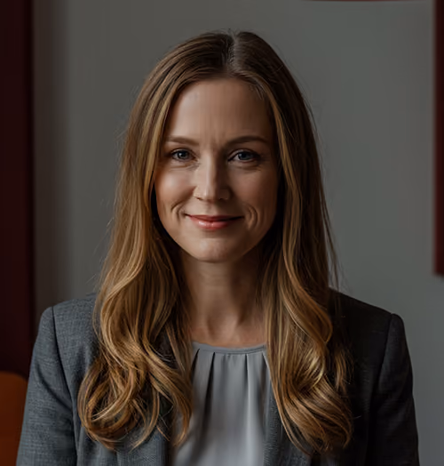 Smiling woman with long blonde hair wearing a gray blazer and light blouse against a muted background.