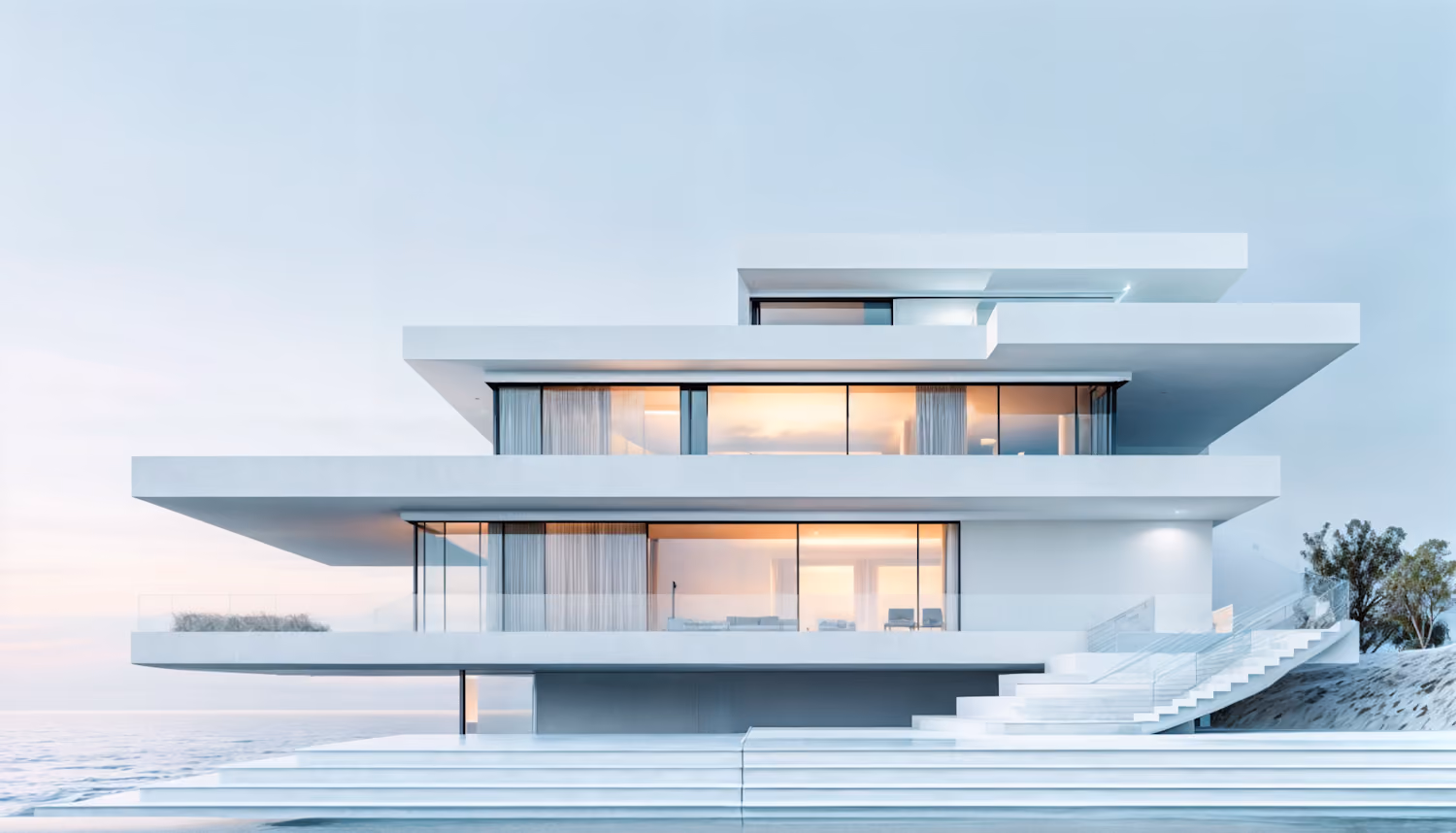 Modern multi-story white house with large glass windows and terraces overlooking water at sunset.