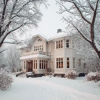 A large white house covered in snow surrounded by bare trees also dusted with snow in a winter landscape.