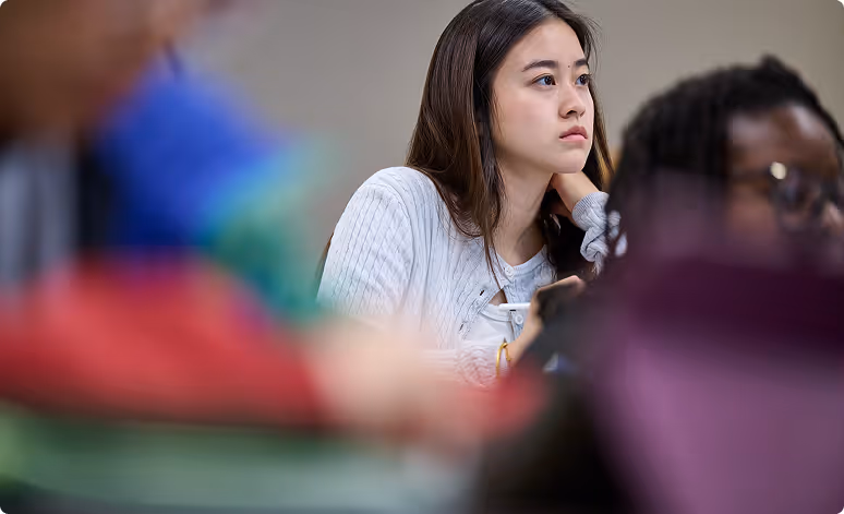 Thoughtful young woman looking to the side in a classroom setting.