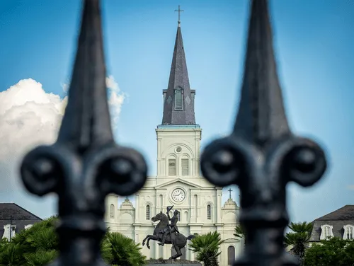 St. Louis Cathedral in New Orleans framed by wrought iron fence with equestrian statue in front.
