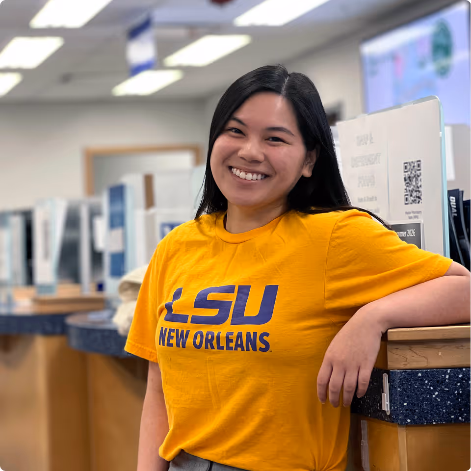 Smiling woman wearing a bright LSU New Orleans t-shirt leaning on a counter in a well-lit office.