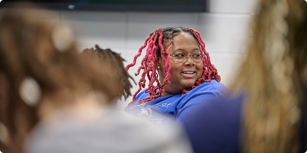 Smiling woman with red braided hair and glasses in a blue shirt among blurred people.