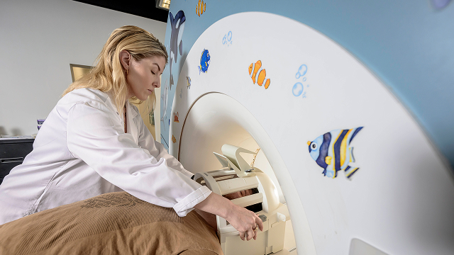 Medical technician adjusts controls on a pediatric MRI machine decorated with colorful fish stickers.