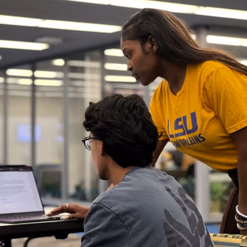 Woman in yellow LSU shirt helping a man with glasses on a laptop in a modern office.