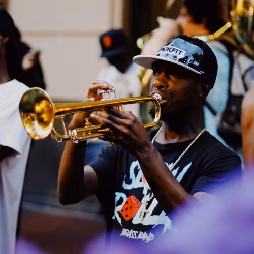 Man wearing a cap plays a golden trumpet during an outdoor musical performance.