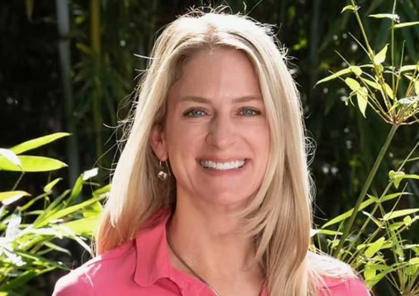 Jeanette Weiland. Smiling woman with long blonde hair wearing a pink top in a leafy outdoor setting.