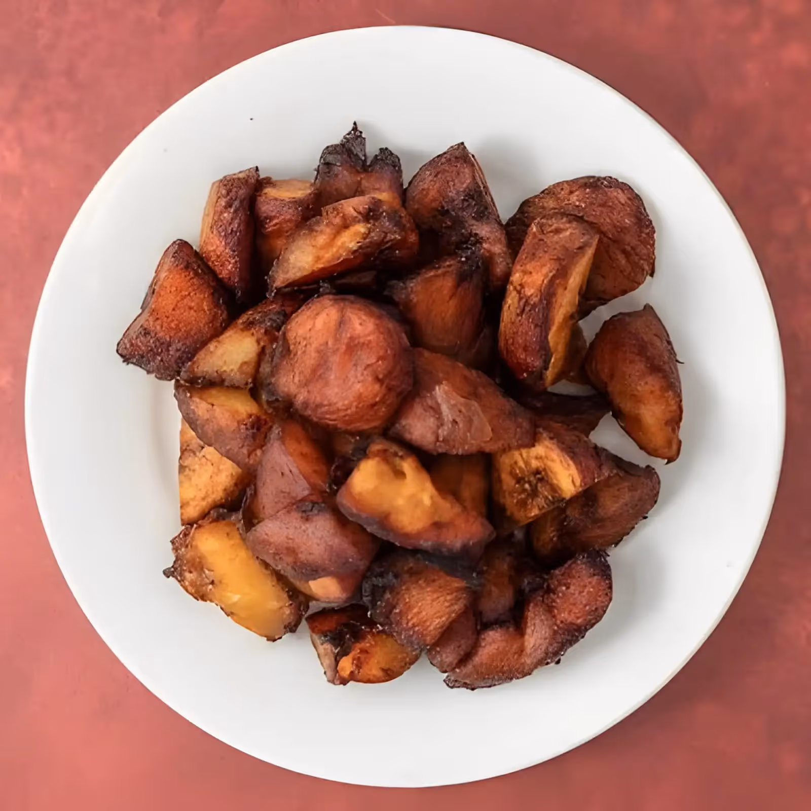 White plate filled with crispy fried plantain pieces on a red surface.