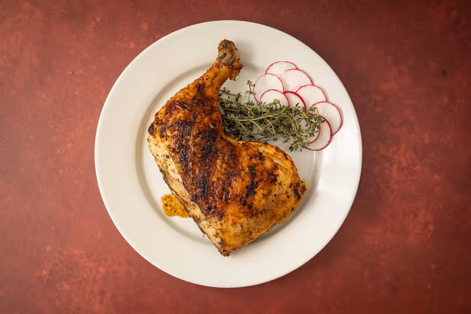 Grilled chicken leg quarter served with fresh thyme and sliced radishes on a white plate.