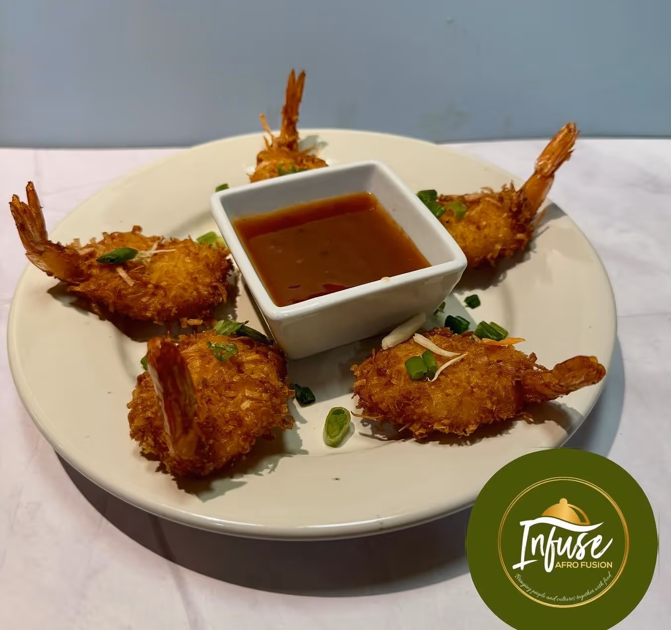 Five crispy fried shrimp with green garnish arranged around a square dish with brown dipping sauce.