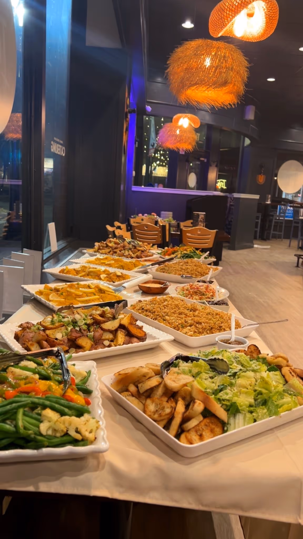 Assorted buffet dishes with vegetables, salad, potatoes, rice, and fruits on a table in a restaurant.